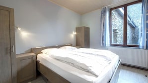 Une chambre à coucher comprenant un lit, une armoire en bois, des tables de chevet et une fenêtre donnant sur un mur en pierre.