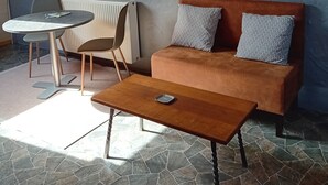 Un salon chaleureux doté d’un sol en pierre, d’un canapé marron agrémenté de coussins à motifs, d’une table ronde avec deux chaises et d’une table basse en bois.