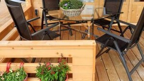 A wooden deck with a glass-top table and four chairs, surrounded by potted plants. - Prive Jacuzzi, Cows, Dairyfarm, Relaxing, Sleeping (Hitzum)
