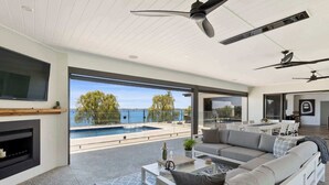 En moderne stue med swimmingpool, ventilatorer i loftet og et stort fjernsyn.
