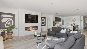 En moderne stue med pejs, sofa og spiseplads i baggrunden.