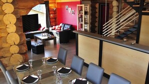 A dining area with a long table set for six, a sofa, and a staircase. - Chalet montagne neuf 4* avec WI FI et jacuzzi 10 personnes plus 2 pers sup (Rencurel)