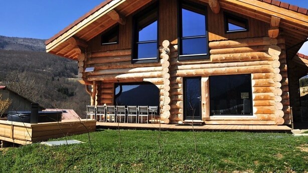 A log cabin with a large deck, multiple windows, and a mountainous backdrop. - Chalet montagne neuf 4* avec WI FI et jacuzzi 10 personnes plus 2 pers sup (Rencurel)