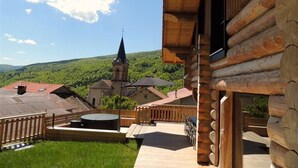 A wooden cabin with a deck, a view of a church with a steeple, and a green landscape in the background. - Chalet montagne neuf 4* avec WI FI et jacuzzi 10 personnes plus 2 pers sup (Rencurel)