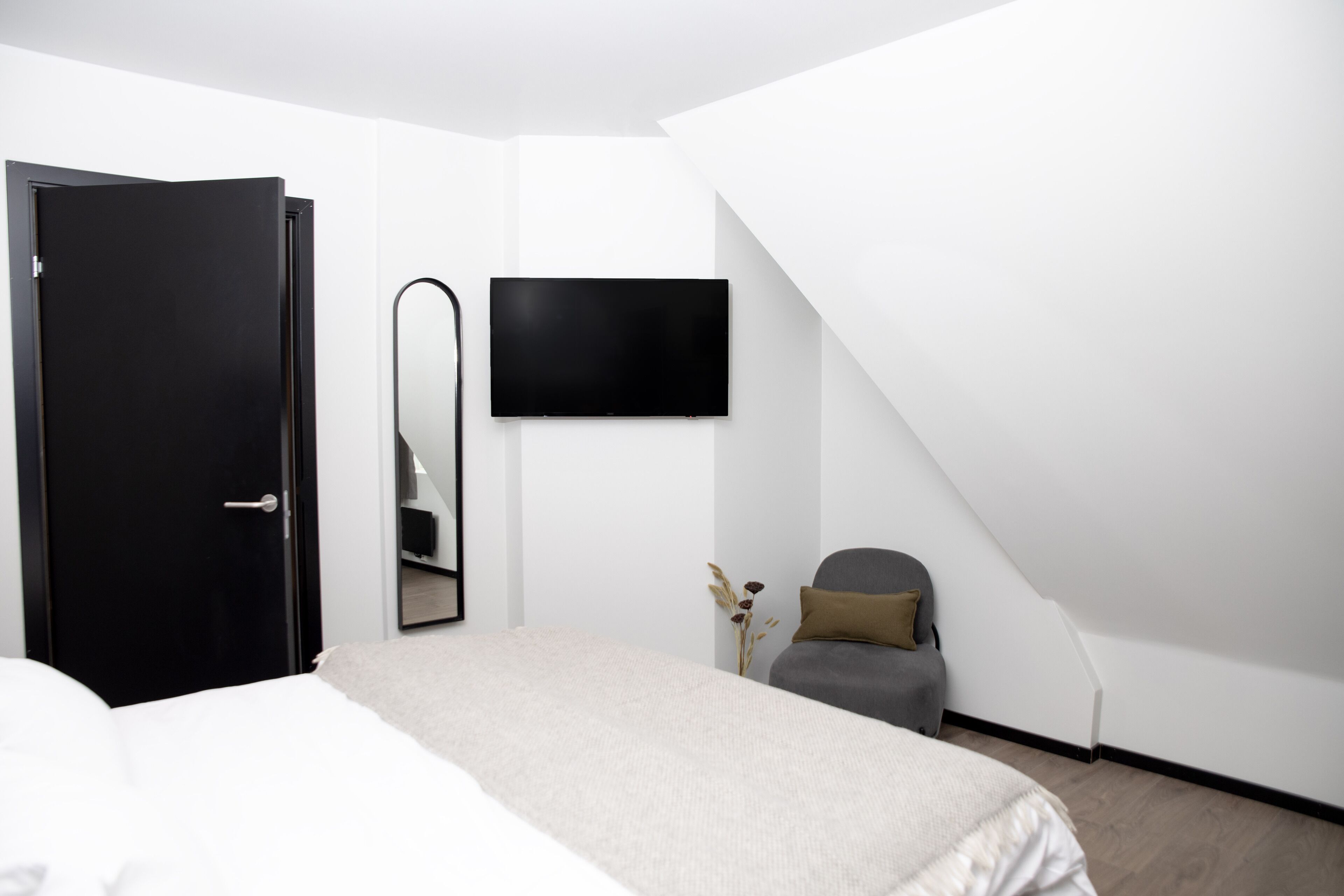 Un dormitorio con cama, una silla, televisor y puerta.