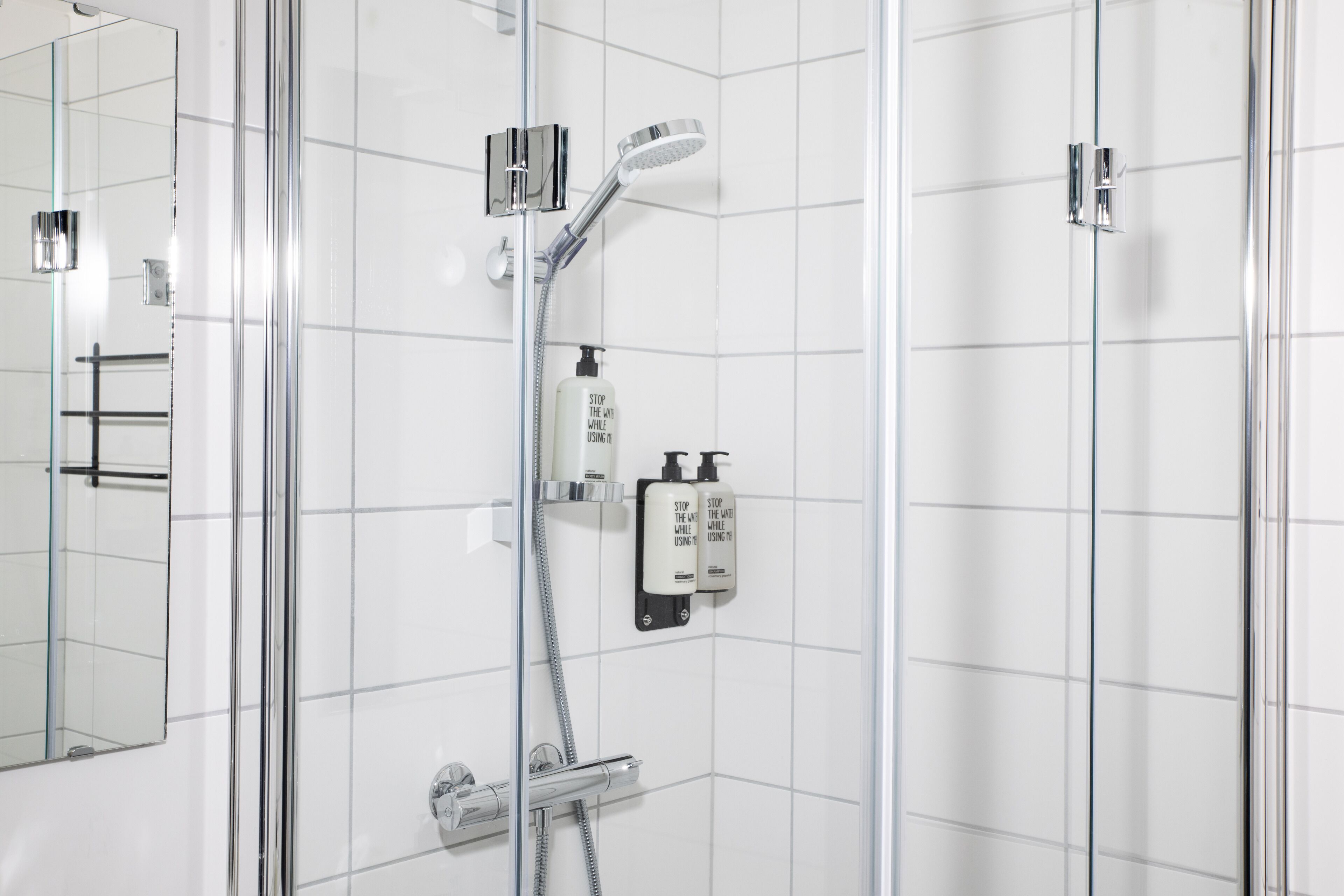 A modern bathroom with a glass shower enclosure, a handheld showerhead, and two soap dispensers mounted on the wall.