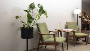 Een kamer met twee groene bekleden stoelen, een klein houten tafeltje en een potplant.