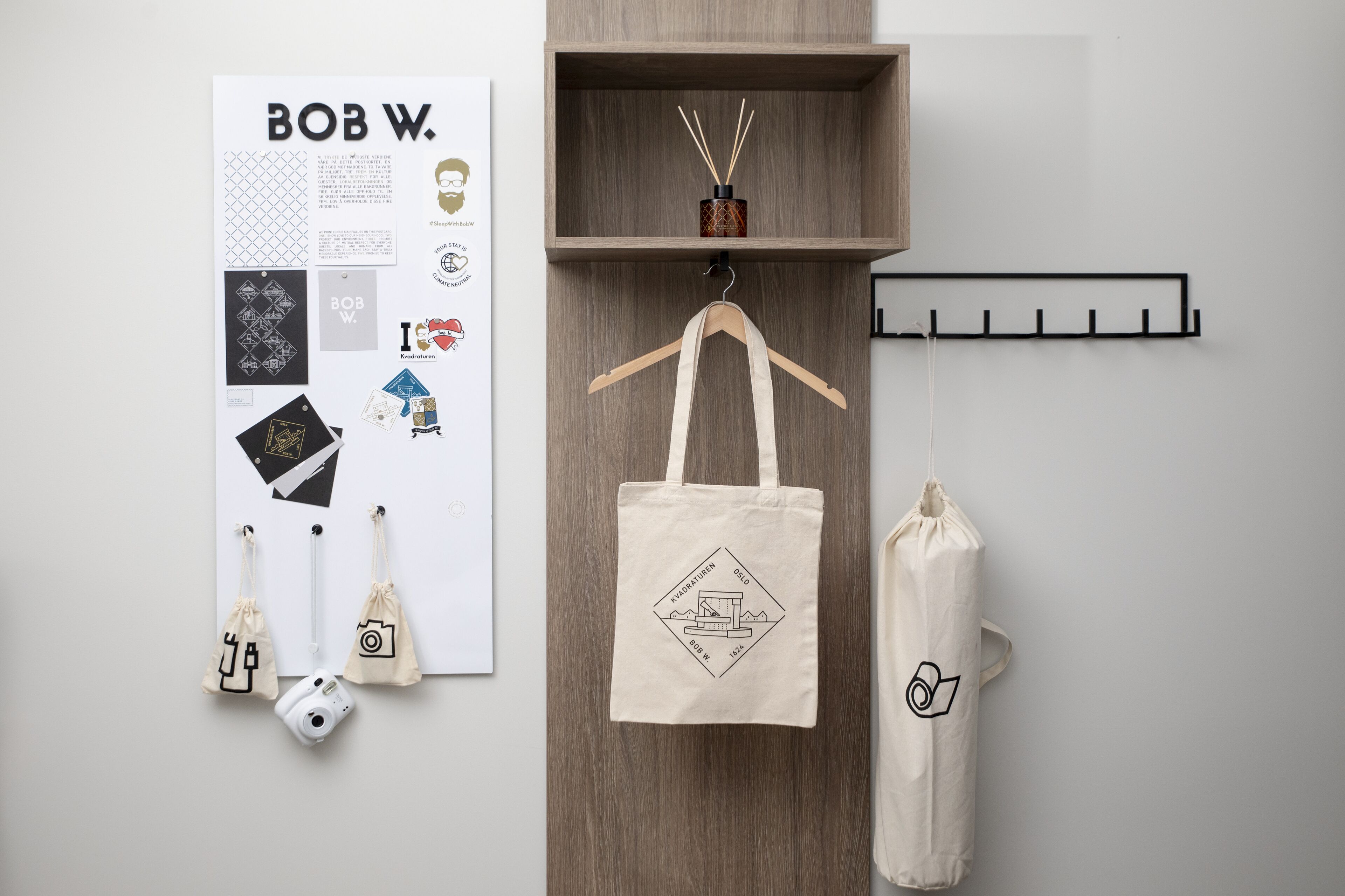 A wall with a poster, a wooden shelf with a diffuser, and a coat rack with bags and a camera.