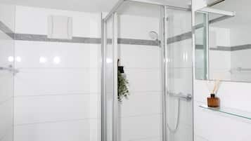 Un baño moderno con azulejos blancos, cabina de ducha de vidrio, repisa de vidrio con un objeto decorativo y un espejo.