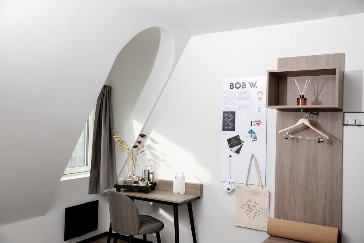 Una habitación moderna con escritorio, silla y armario de madera. Hay un póster en la pared y una ventana con cortinas.
