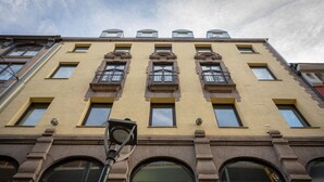Een meerlaags gebouw met een gele gevel, grote ramen en een opvallende ingang met een donkere deur.
