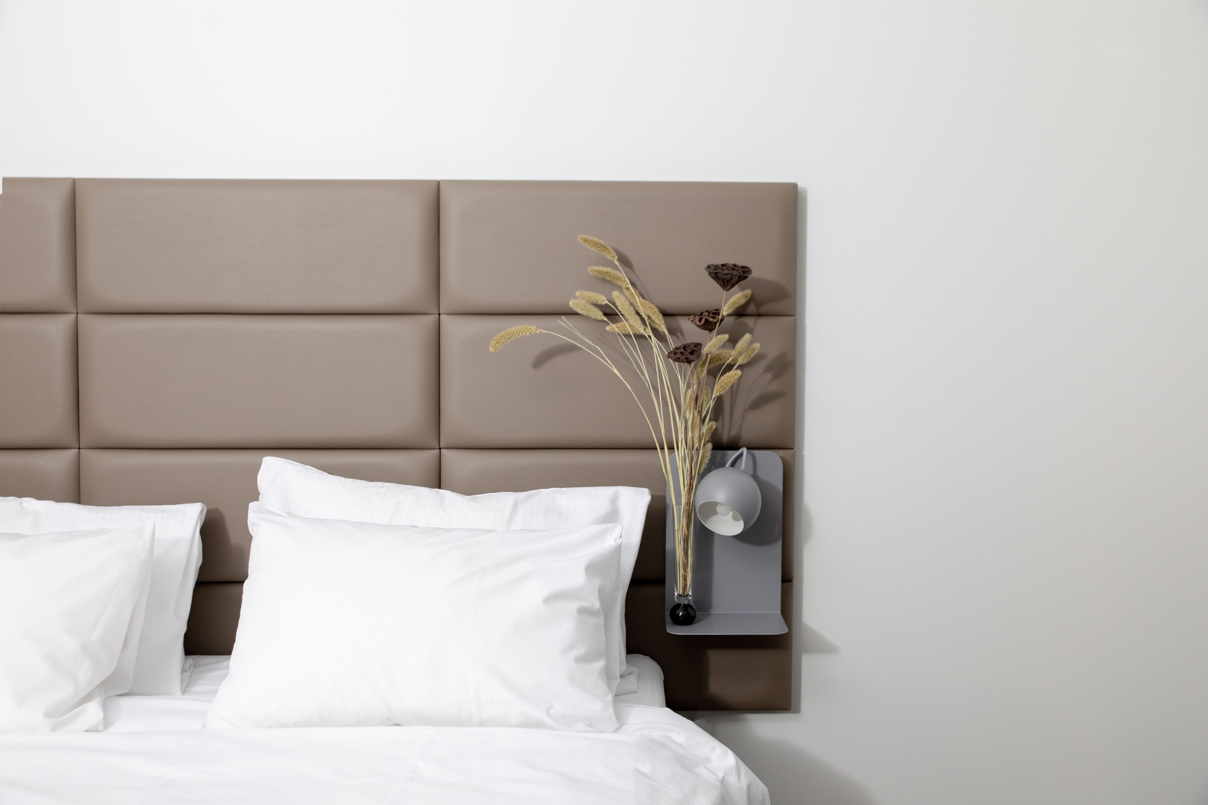 Cama bem arrumada com roupa de cama branca e cabeceira com design acolchoado.