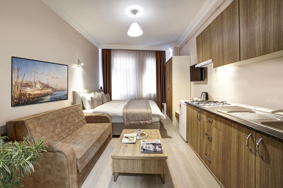 Quarto de hotel compacto com cama, sofá, cozinha compacta e pintura de um horizonte urbano.