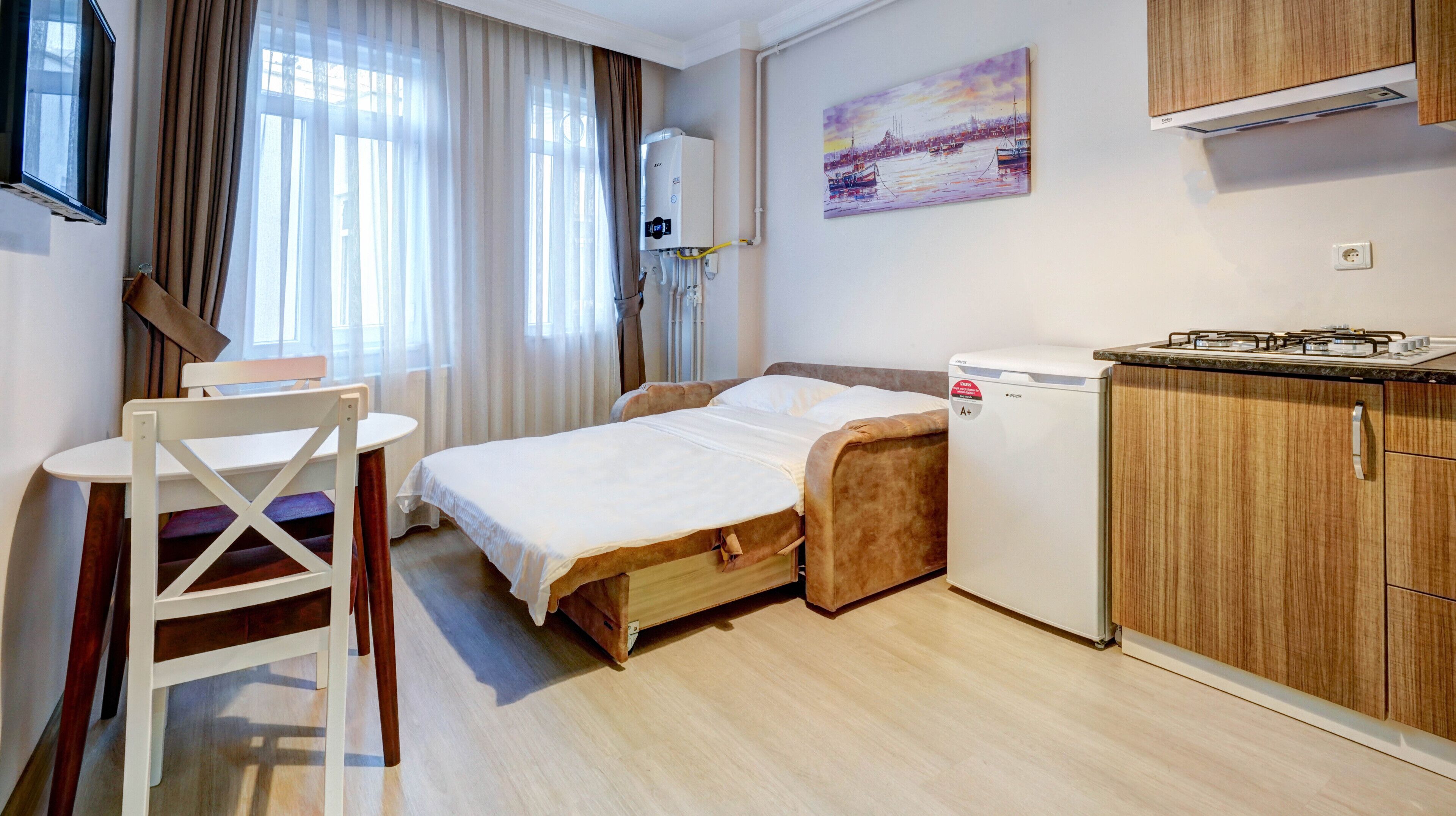 Habitación de hotel compacta con cama, pequeña kitchenette, zona de comedor con mesa y silla, y un cuadro en la pared.