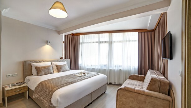 A modern hotel room with a large bed, a sofa, a flat-screen TV, and a window with curtains. - Seven Roses Apart Hotel (Istanbul)