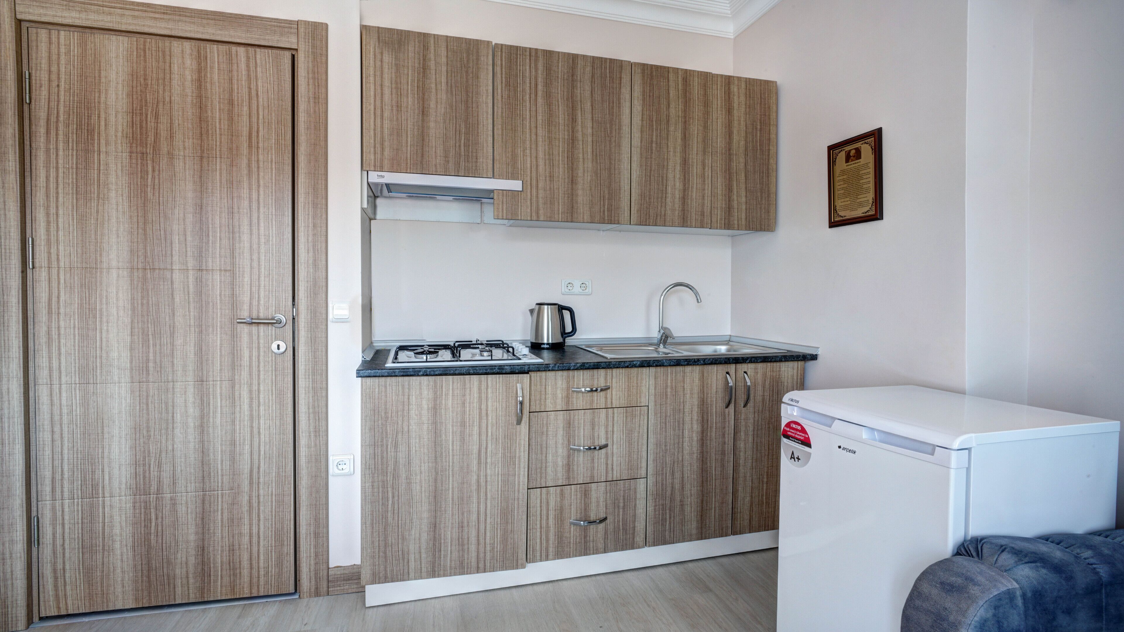 A compact kitchen with wooden cabinets, a gas stove, a kettle, and a small refrigerator.
