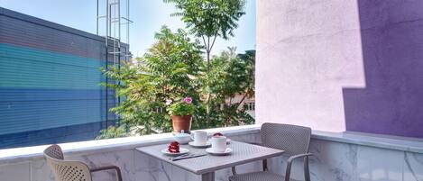 Un balcón con una mesa dispuesta para dos personas, una planta en maceta y vistas a un edificio.