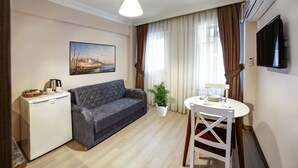 A modern living room with a grey sofa, a small white table with a lamp, a coffee machine, and a painting on the wall. - Seven Roses Apart Hotel (Istanbul)