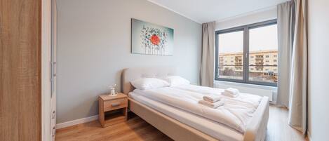 A neatly made bed with white linens and a small bedside table with a lamp. A painting of flowers hangs above the bed.