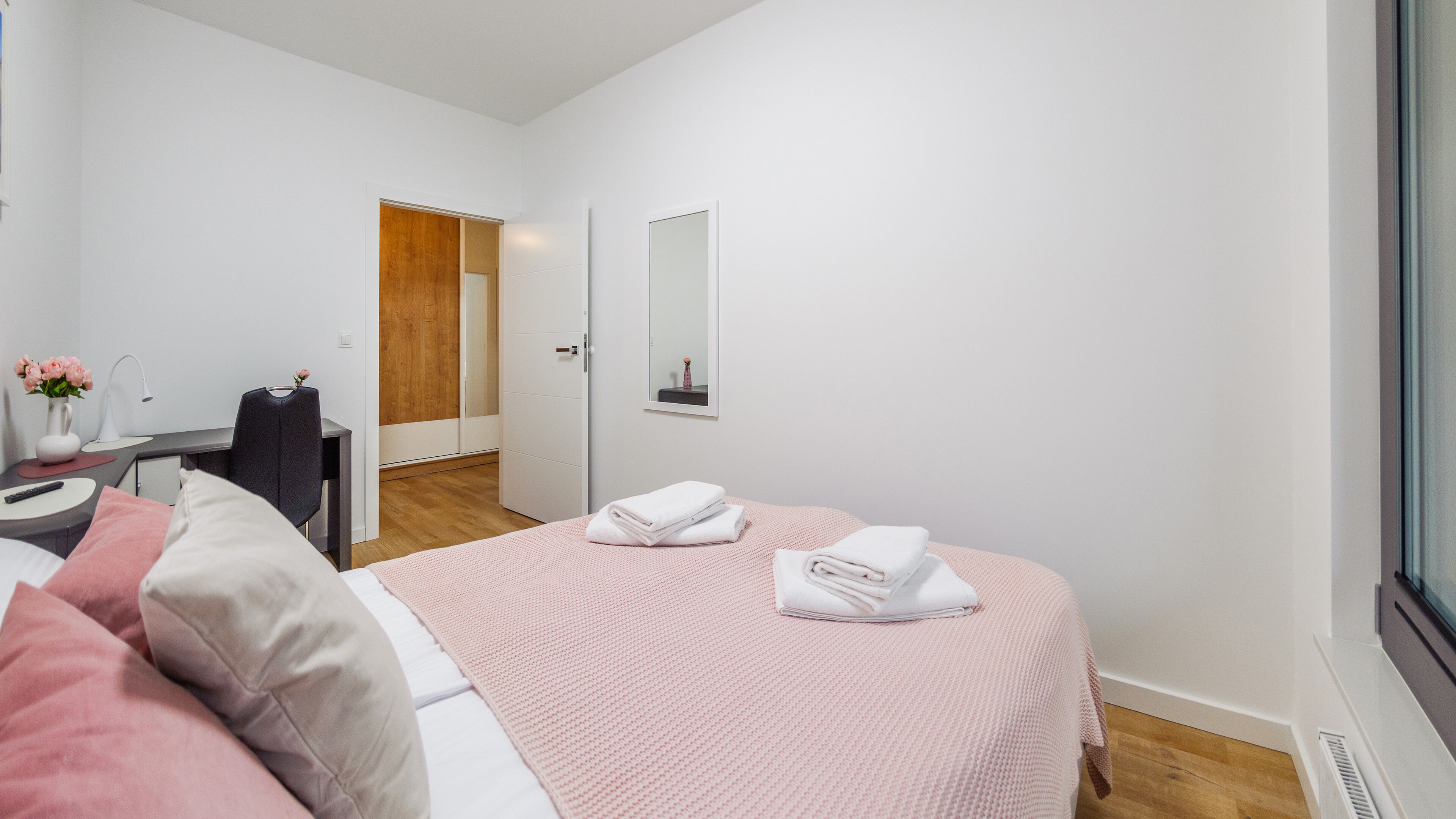 A modern bedroom with a bed, bedside table, and a mirror.