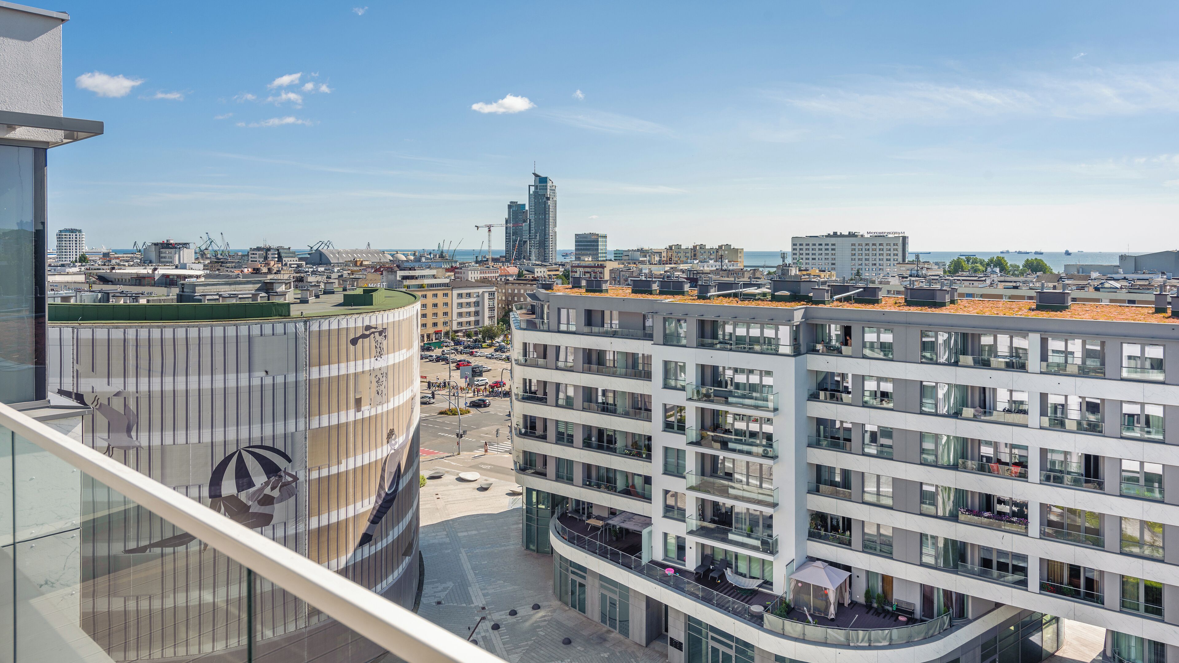 Ein modernes Gebäude mit mehreren Etagen, großen Fenstern und einer Dachterrasse mit Außenbestuhlung.