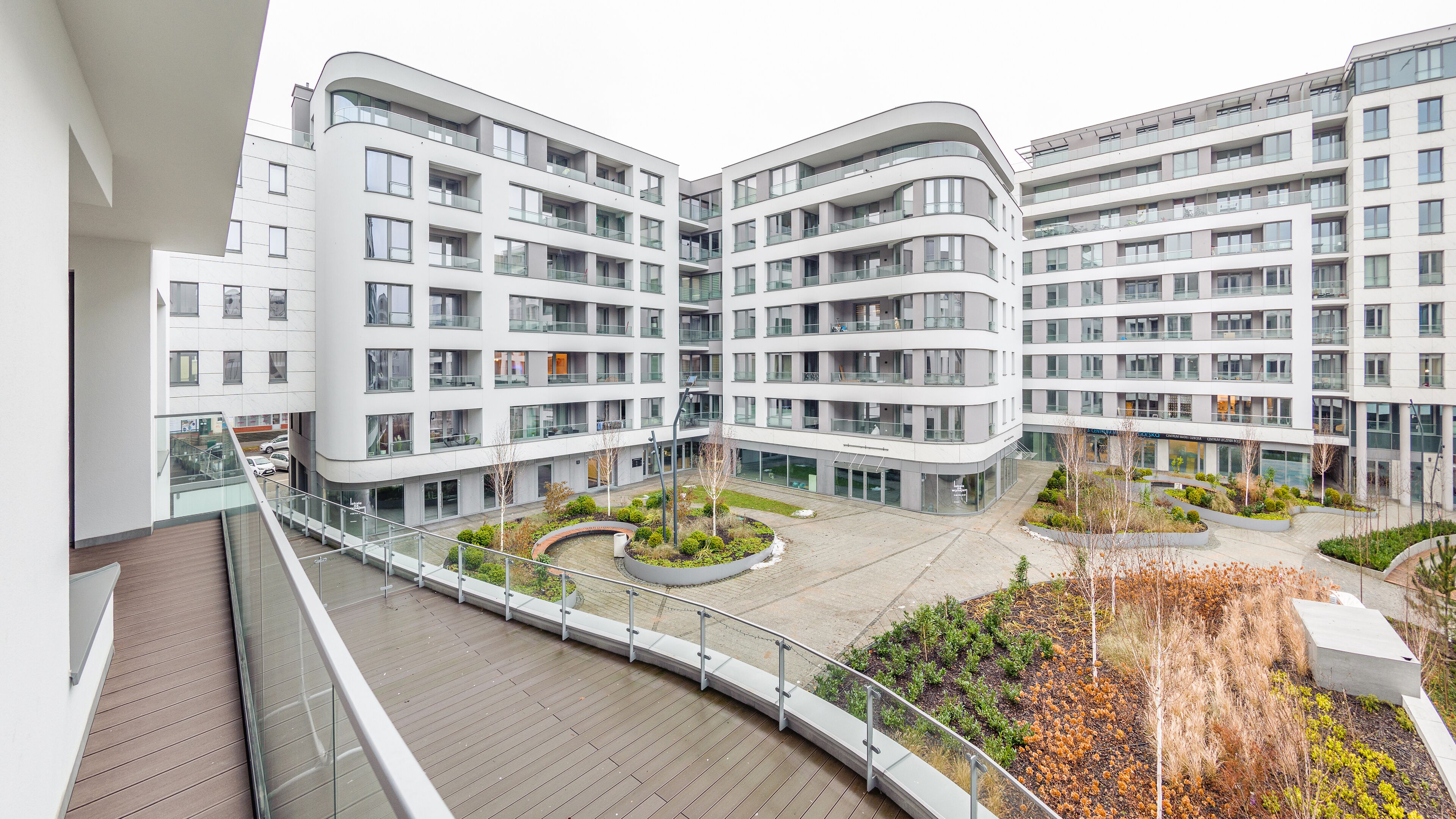 A modern apartment complex with multiple balconies, a central courtyard with landscaping, and a view from a balcony.