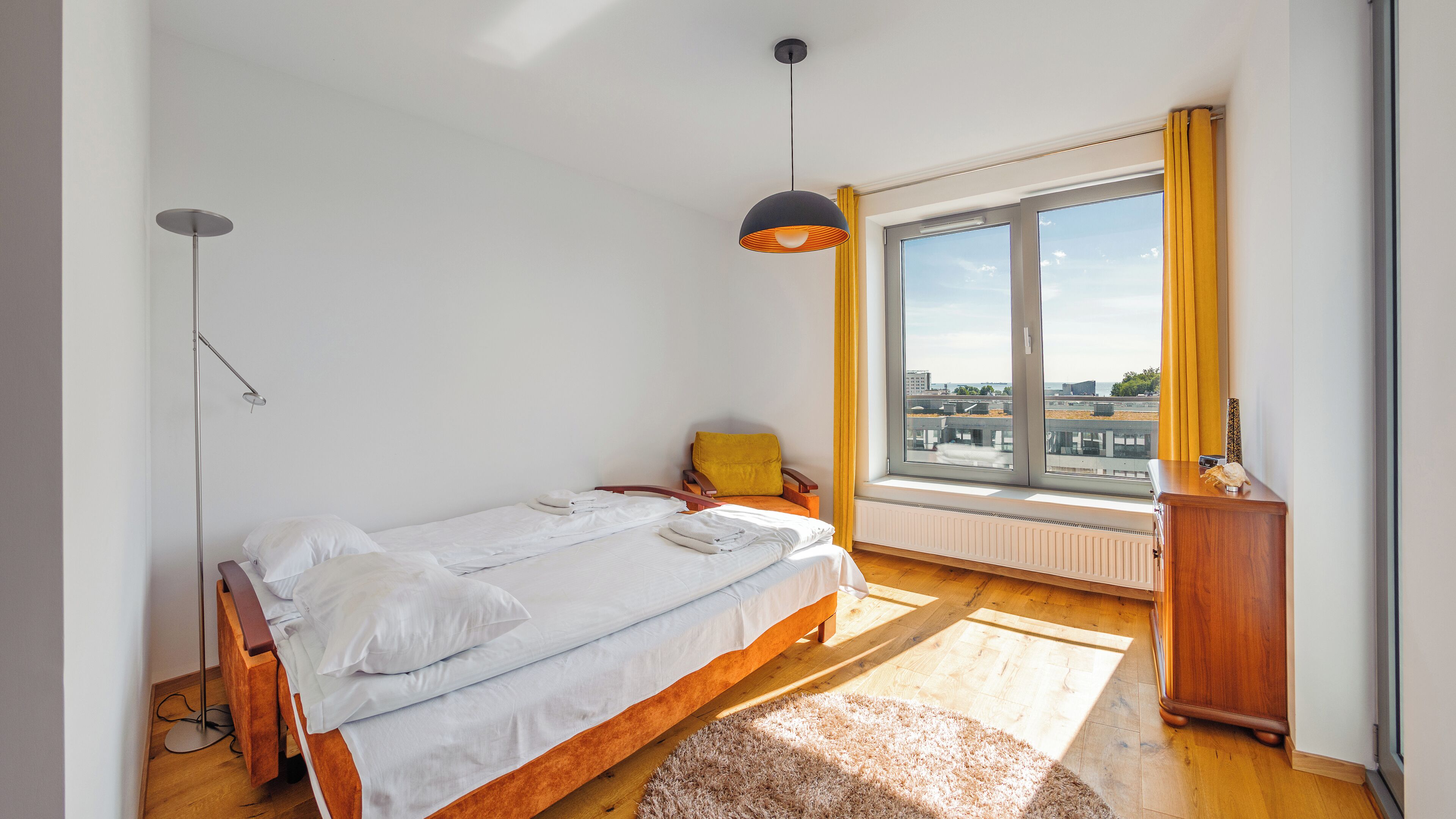 Une chambre à coucher avec un lit, une chaise, un bureau, une fenêtre et un radiateur.
