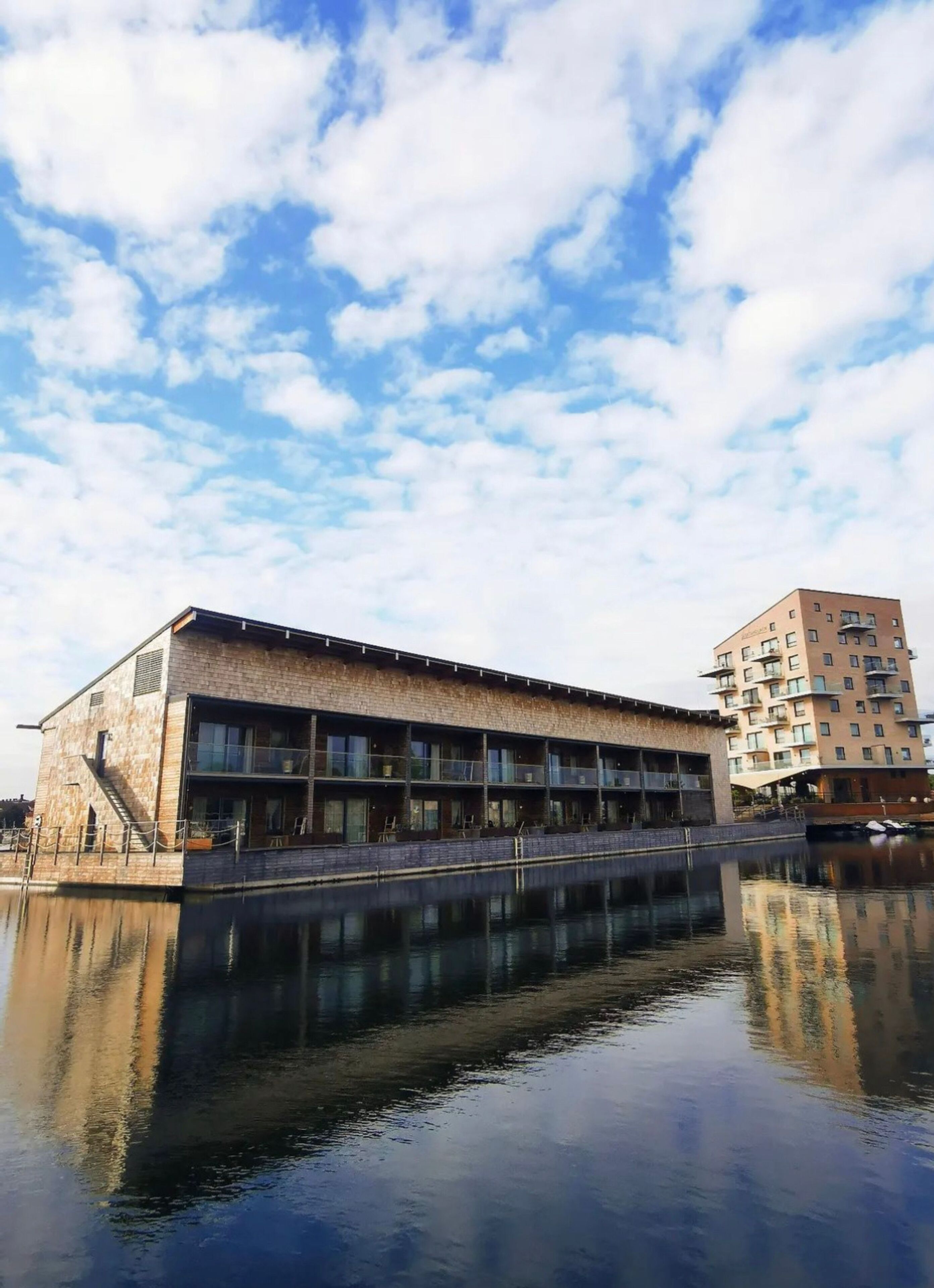 A waterfront building with a reflective pool, featuring a long, narrow structure with multiple balconies and a brick facade.