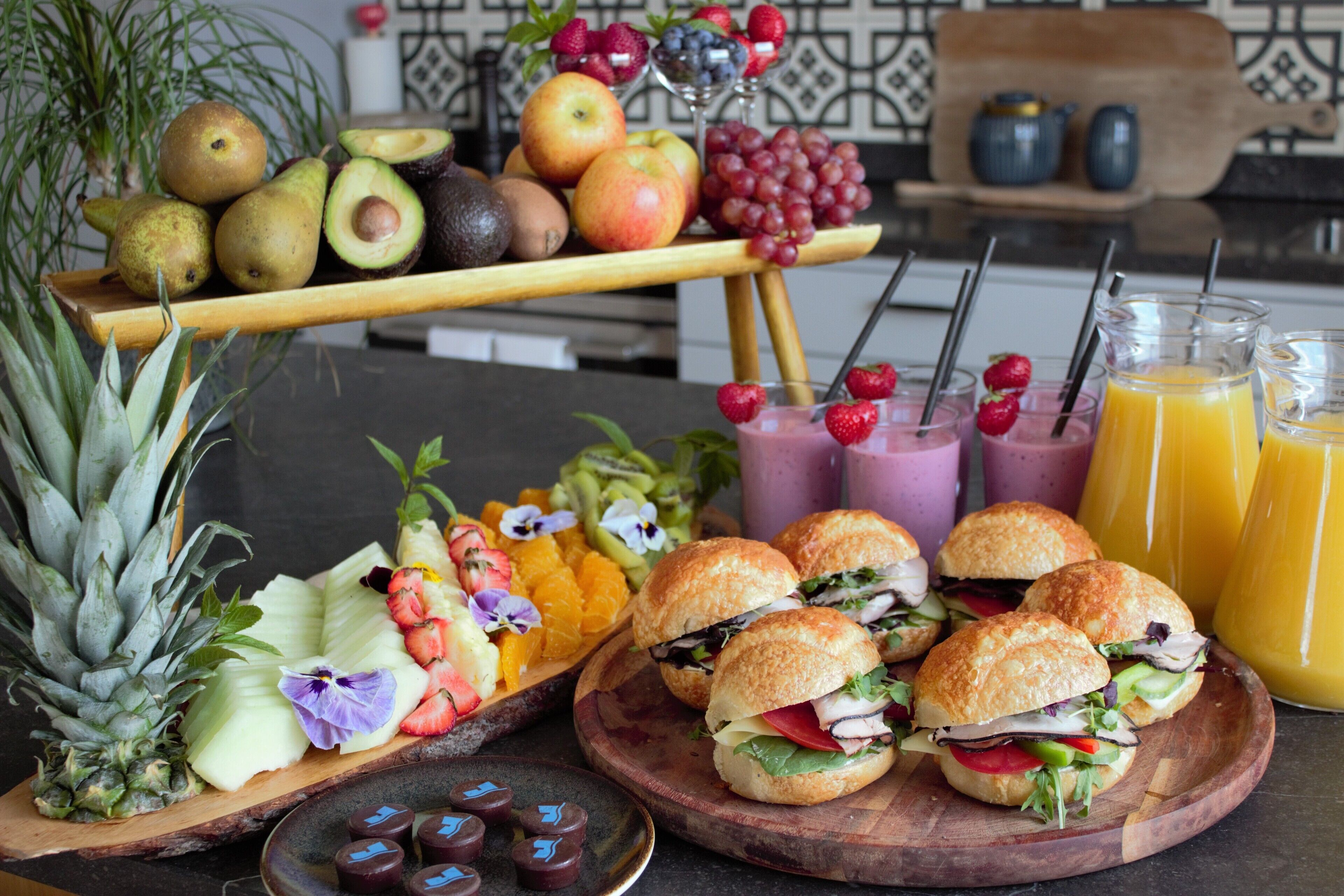 A fruit platter with various fruits, sandwiches, and drinks on a table.