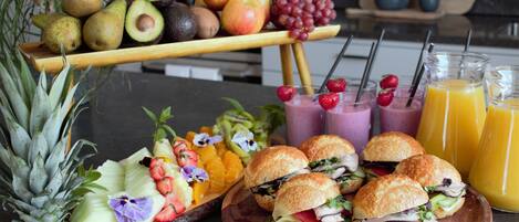 A fruit platter with various fruits, sandwiches, and drinks on a table.