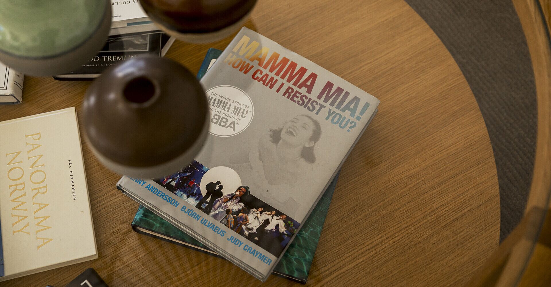 A book titled 'Mamma Mia! How Can I Resist You?' on a wooden table with a round tablecloth.