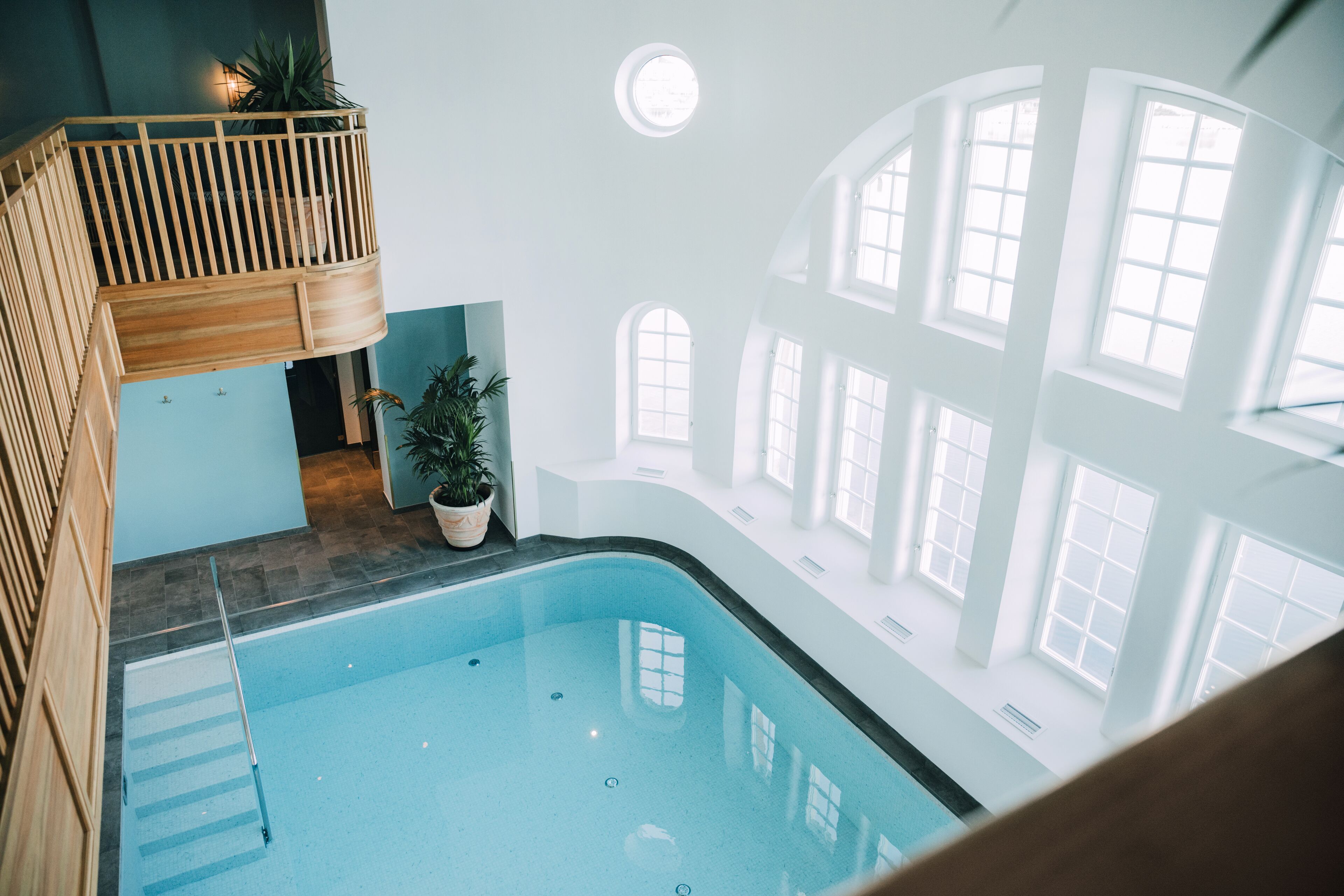 An indoor swimming pool with a wooden deck and potted plants.