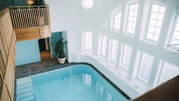 An indoor swimming pool with a wooden deck and potted plants.