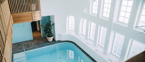 An indoor swimming pool with a wooden deck and potted plants.