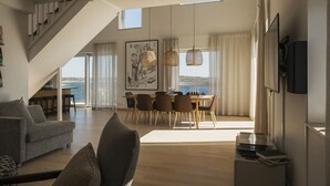 A spacious living area with a staircase, a dining table with chairs, and a large window overlooking a body of water. - Slottsholmen hotell och restaurang (Vastervik)