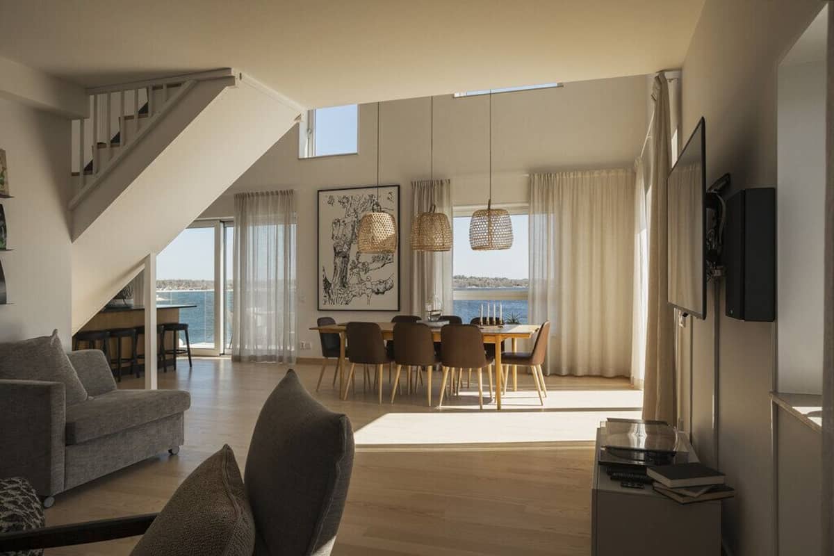 A spacious living area with a staircase, a dining table with chairs, and a large window overlooking a body of water.