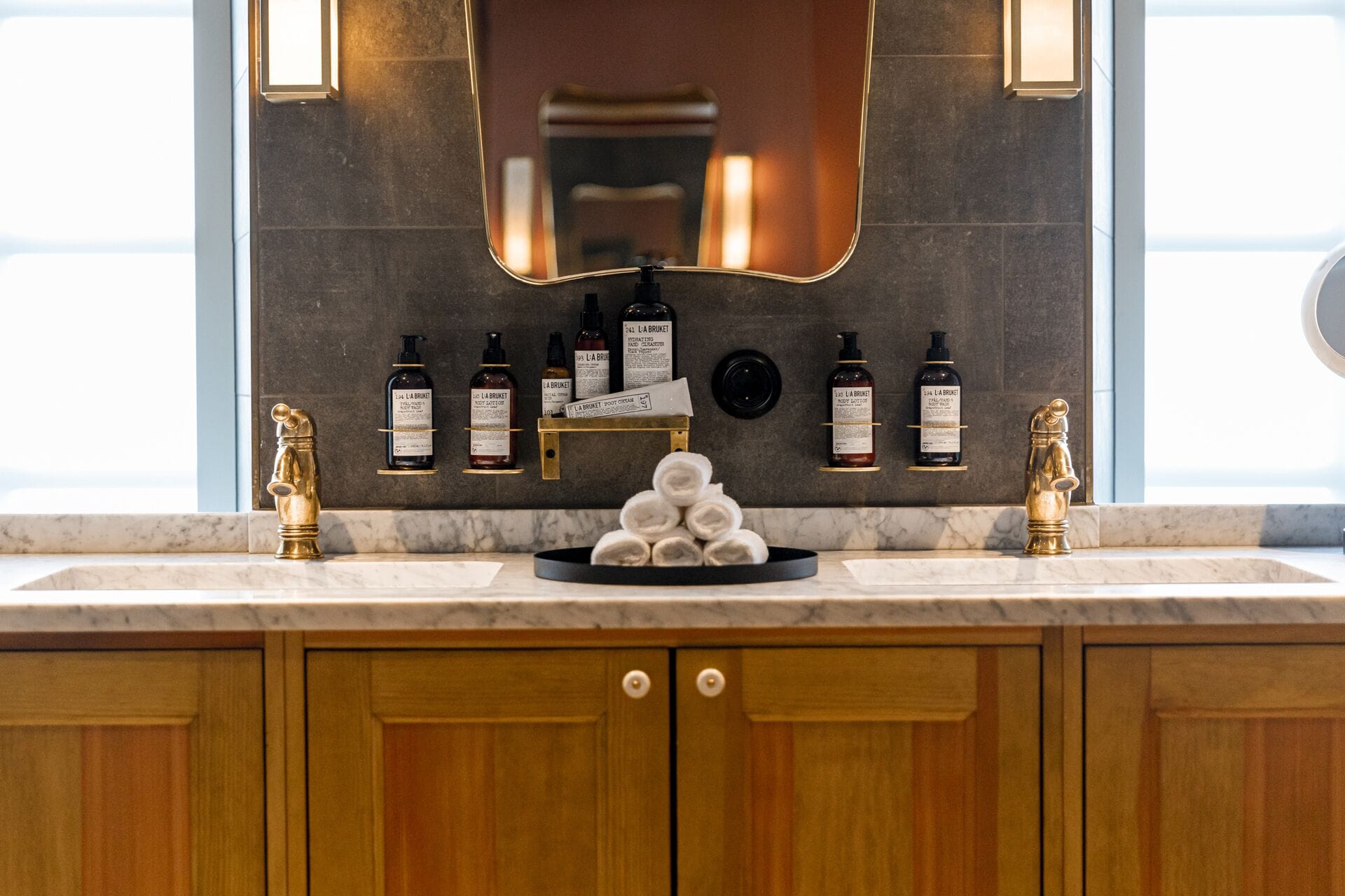 A bathroom with a marble countertop, a sink, a mirror, and toiletries on a shelf.