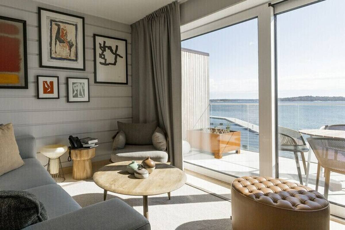A modern living room with a sofa, armchairs, a round coffee table, and a view of the sea through large windows.