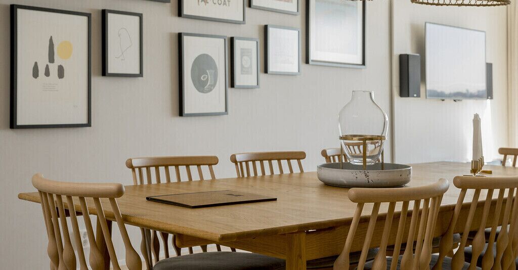 Een eetgedeelte met een houten tafel en stoelen, kunstwerken aan de muur en een vaas op tafel.