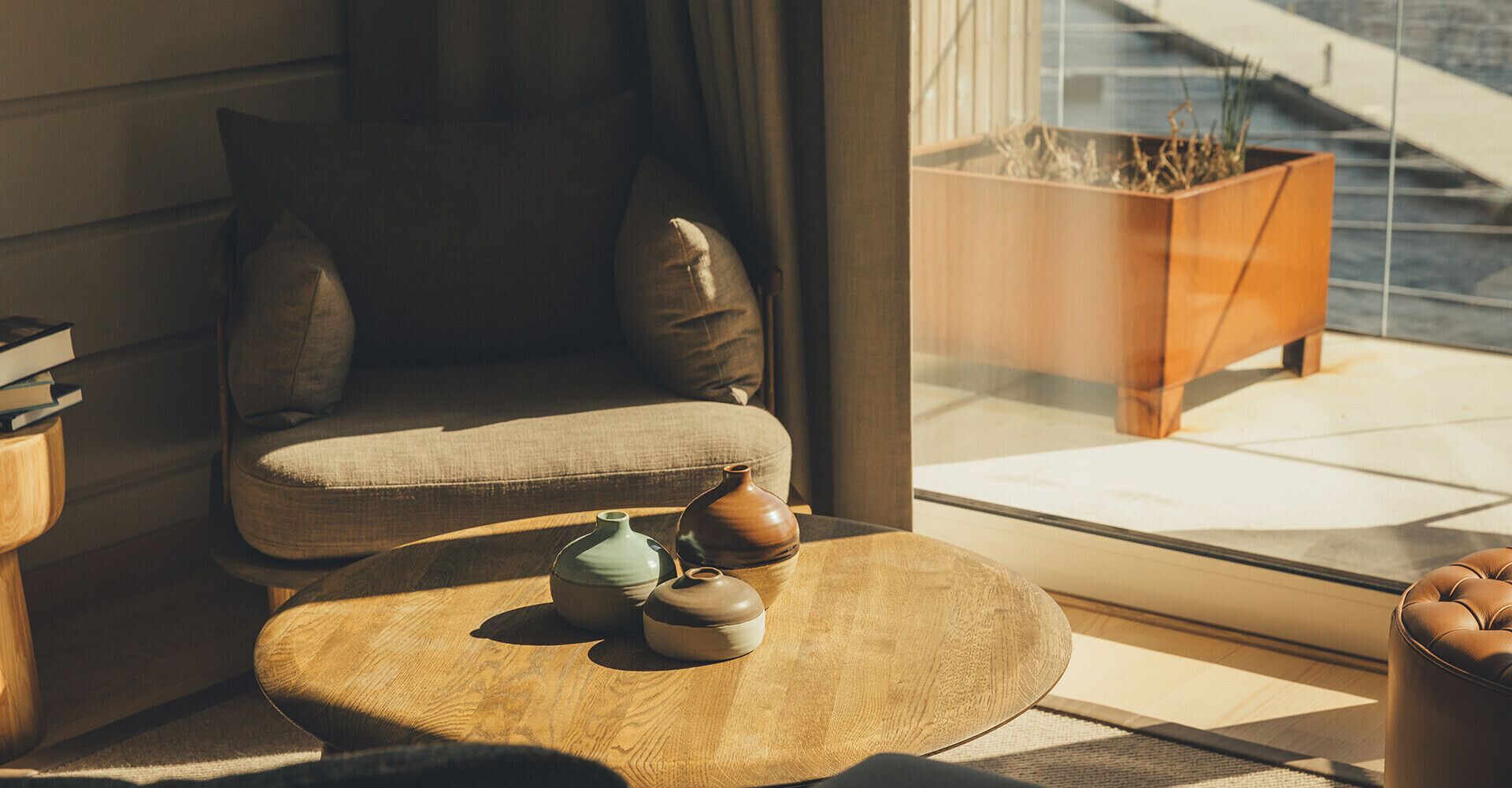 Una sala de estar moderna con un sofá, una mesa de centro con jarrones decorativos y vistas a un edificio a través de una ventana.