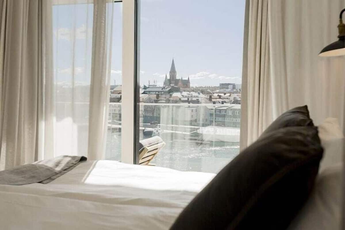 A bedroom with a large window, a bed, and a view of a cityscape.