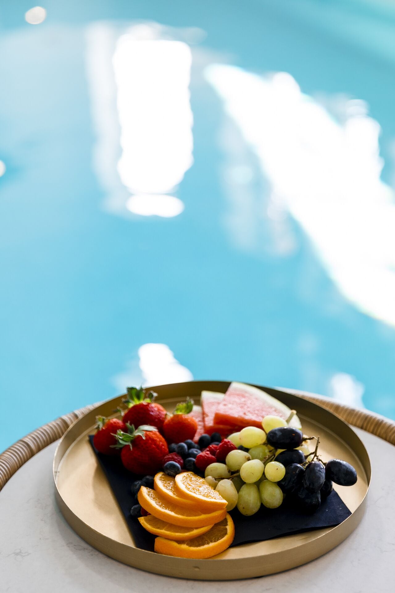 A tray of assorted fruits including strawberries, blueberries, grapes, and watermelon slices, placed on a table by a pool.