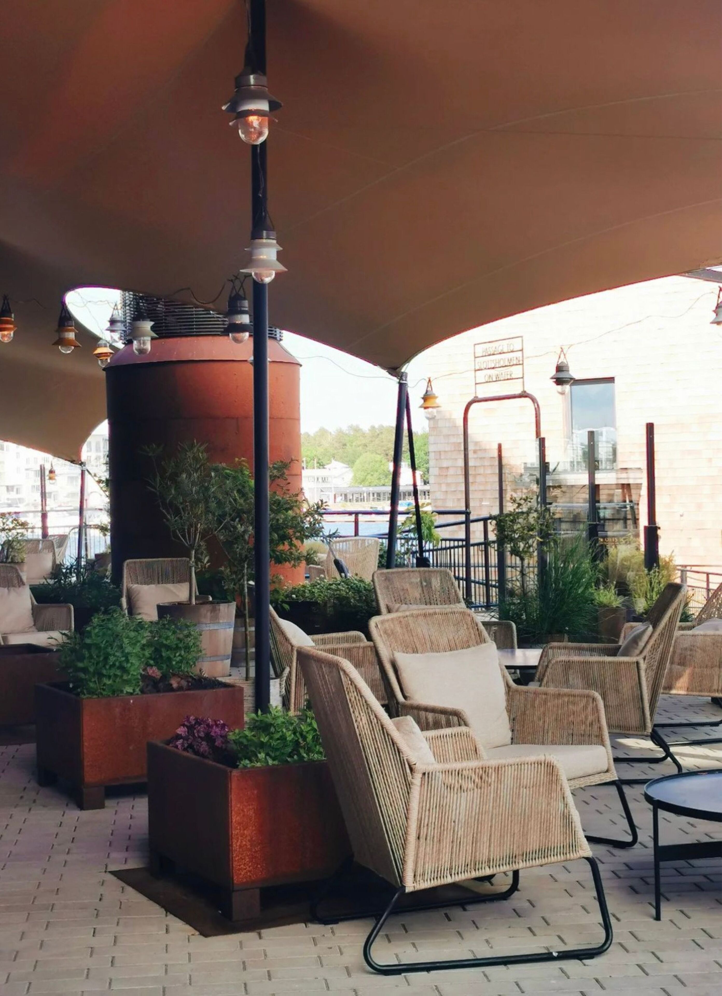 An outdoor seating area with wicker chairs and planters, a large cylindrical structure, and a sign indicating a men's restroom.