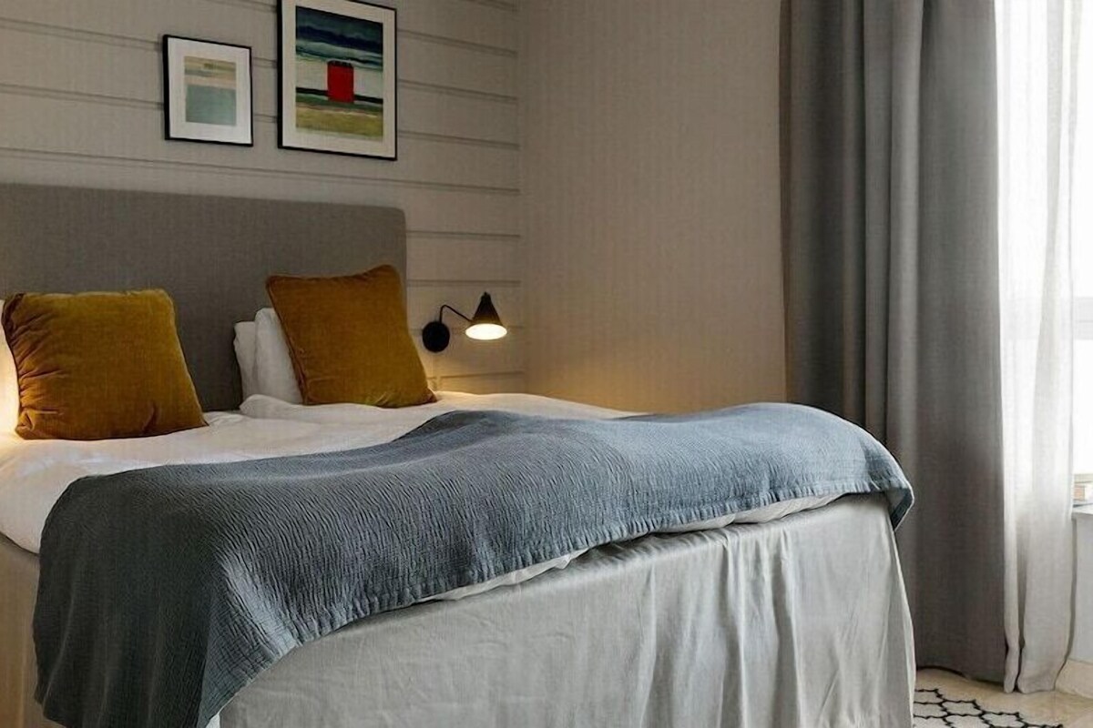A neatly made bed with a grey headboard, two bedside lamps, and a small wooden stool.