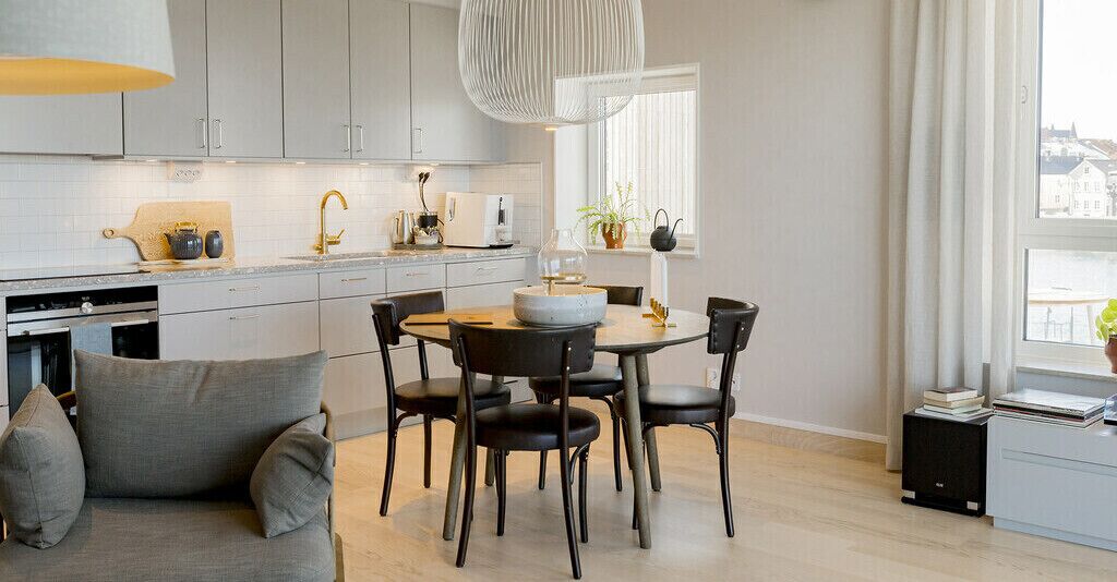 A modern kitchen with grey cabinets, a dining table with black chairs, and a sofa with grey cushions.