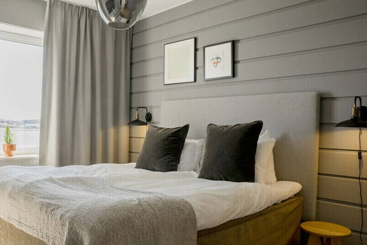 A modern hotel room with a large bed, a bedside table, a lamp, and a view of the water.