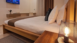 A modern hotel room with a large bed, a TV mounted on the wall, a bedside table with a lamp, and a wooden nightstand. - Sveltos Residence 3Bedroom Suites (Larnaca)
