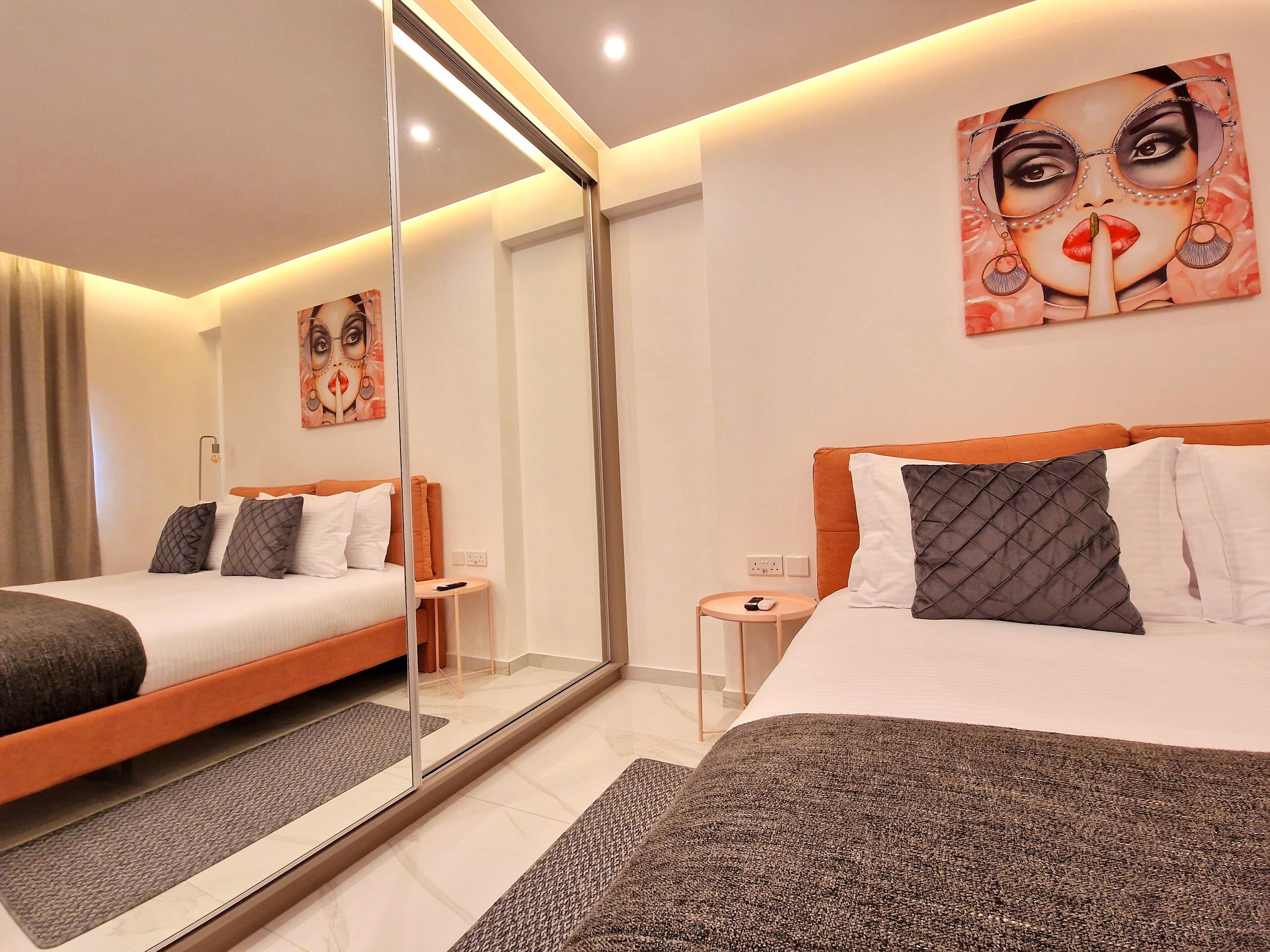 A modern hotel room with a large bed, a small bedside table, a mirror, and a painting on the wall.