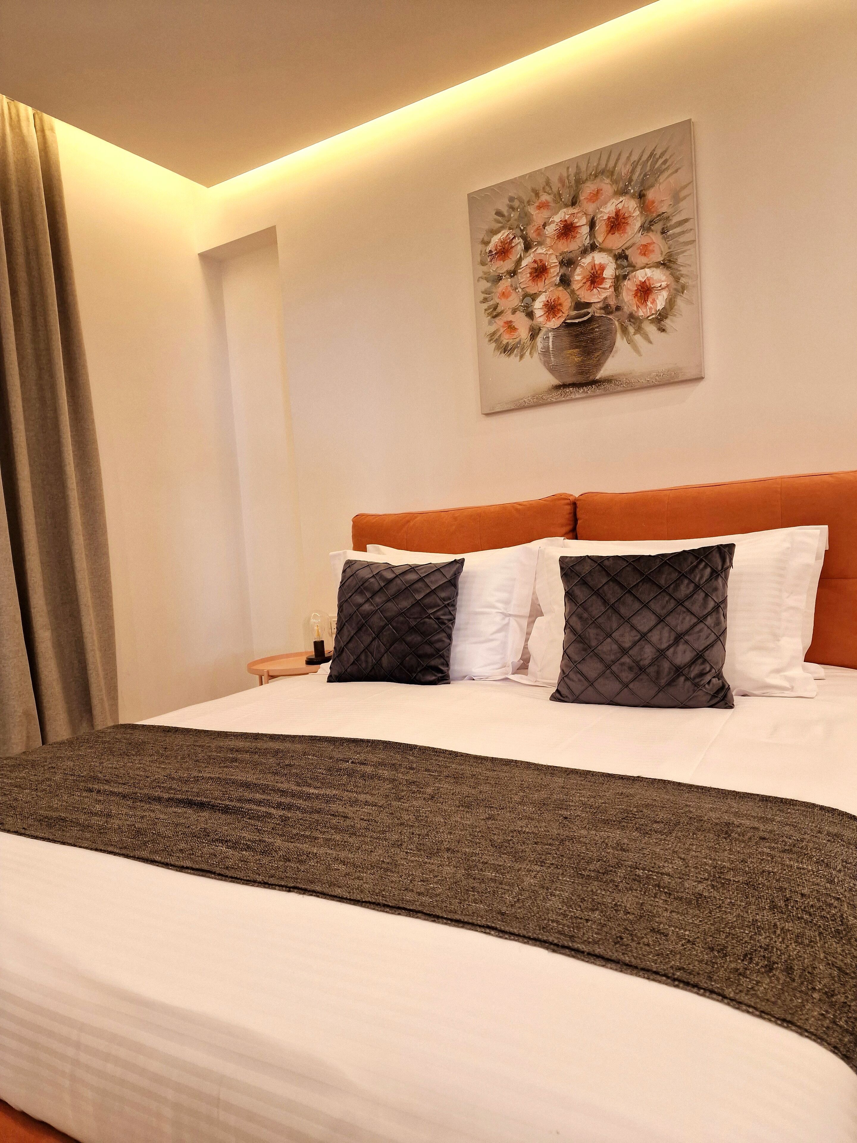 Una cama bien hecha con una manta marrón, almohadas blancas y un cabecero naranja.