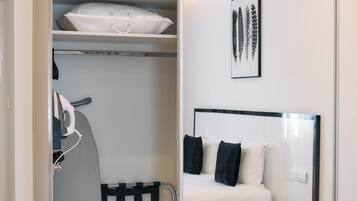 A modern hotel room with a walk-in closet, a bed with black and white bedding, a small round table, and a framed artwork on the wall.